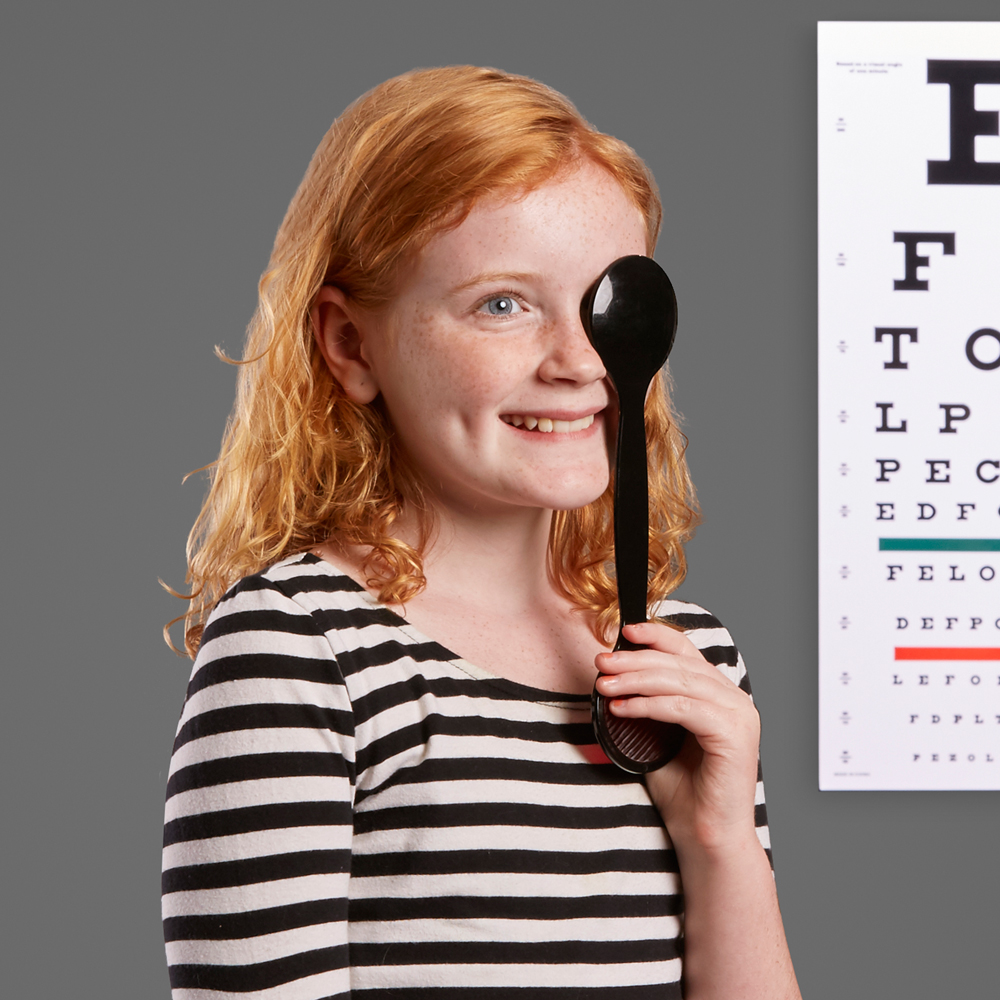 Child using an eye occluder for a vision test with an eye chart in the background.