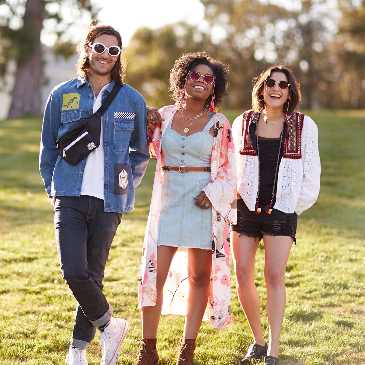 Three individuals in casual and trendy outfits; a denim jacket and fanny pack, a floral kimono over a dress, and a white embroidered jacket.
