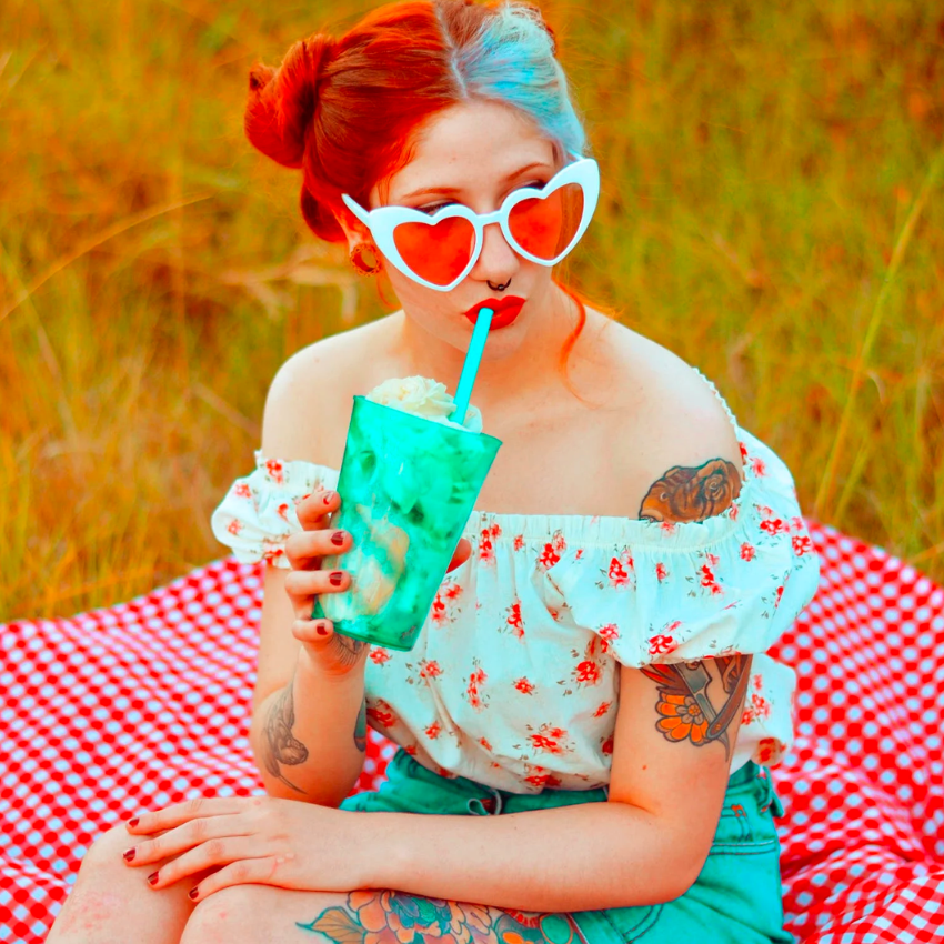 Woman drinking from a turquoise cup with a blue straw, sitting on a red checkered blanket.