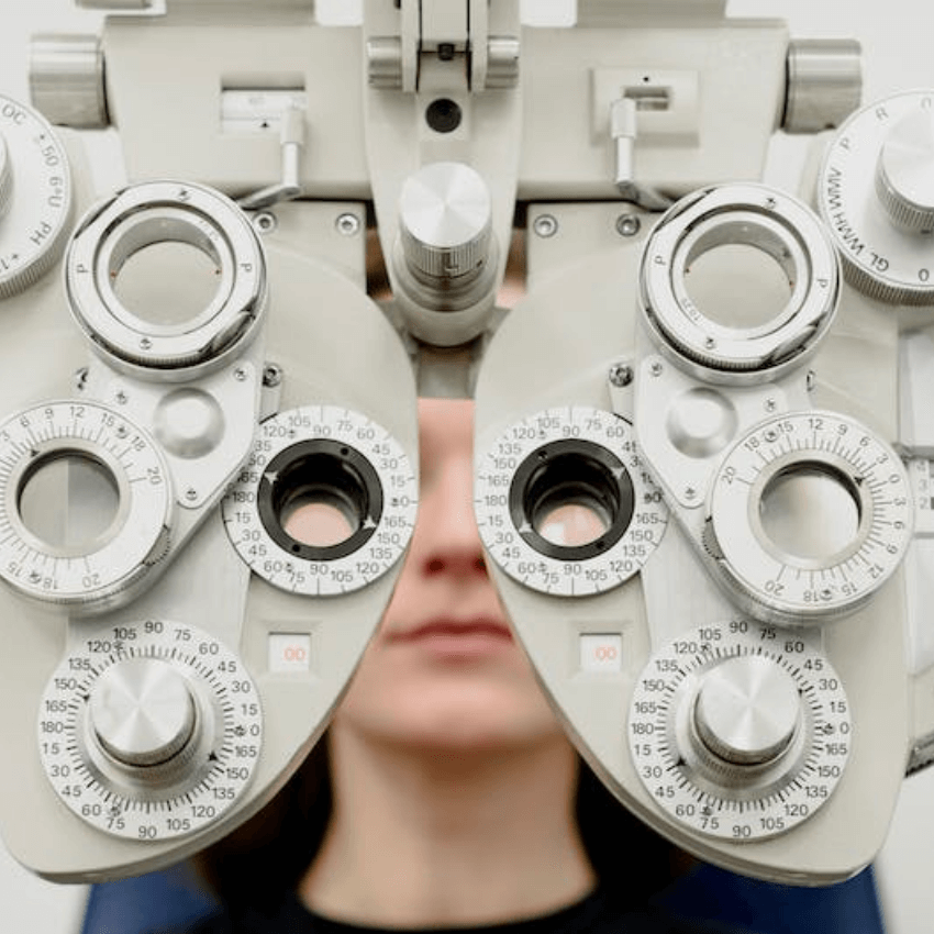 Phoropter for eye exams with various dials and lenses, positioned in front of a person's face.