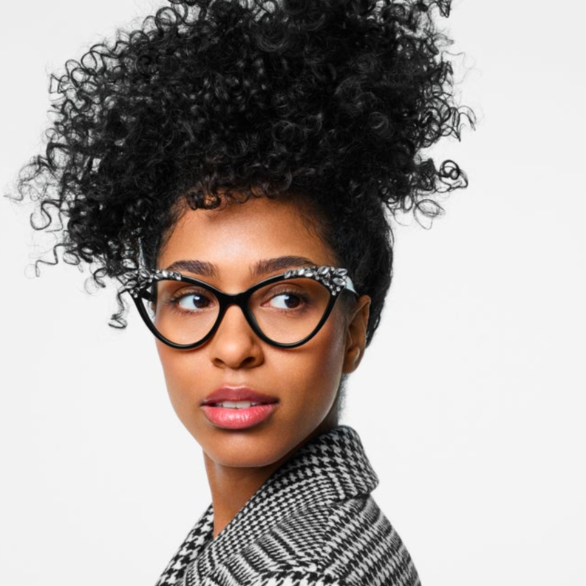 Black cat-eye glasses with white floral detailing on the upper frame worn by a person with curly hair.