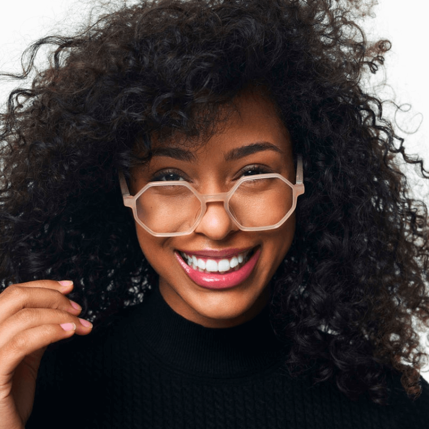 Woman wearing octagon-shaped, clear-framed glasses and a black turtleneck, smiling.