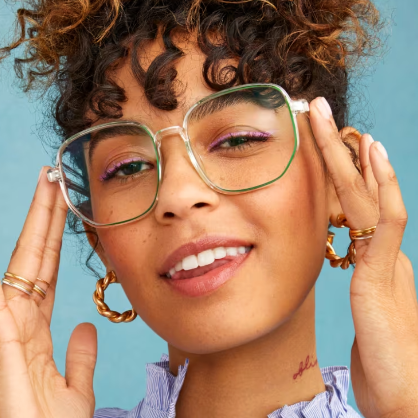 Clear, oversized eyeglasses with a transparent frame and gold accents being adjusted by a person.