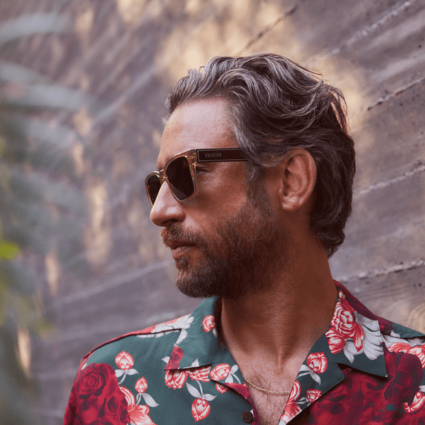 Man wearing dark sunglasses with "ZEGNA" on the temples, dressed in a floral-patterned shirt.