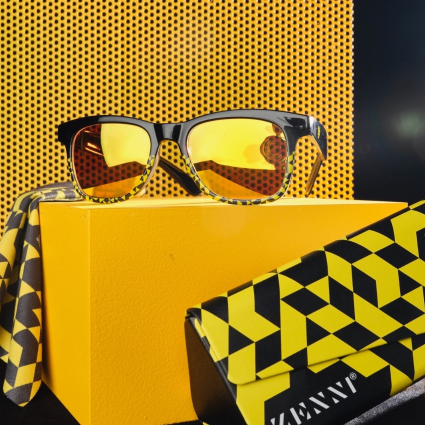 Black-framed sunglasses with yellow lenses, geometric patterned yellow cloth and case with "ZENNI" logo.