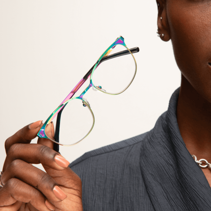 Person holding multicolored eyeglasses with transparent lenses and black temples.