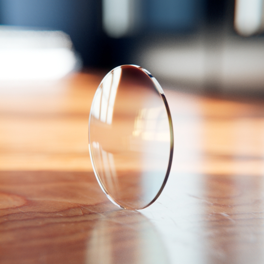 Thin, transparent optical lens standing upright on a wooden surface.