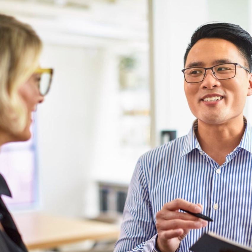 Man in striped shirt talking and smiling while holding a pen and a document. Woman facing him.