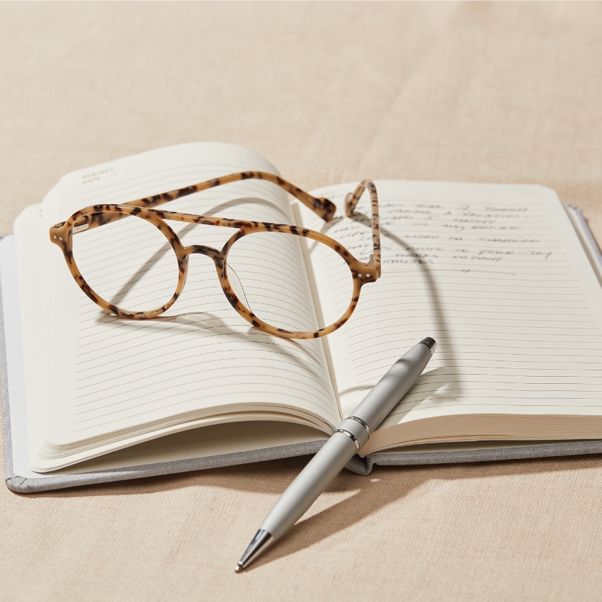 Tortoiseshell glasses and silver pen on an open lined notebook.