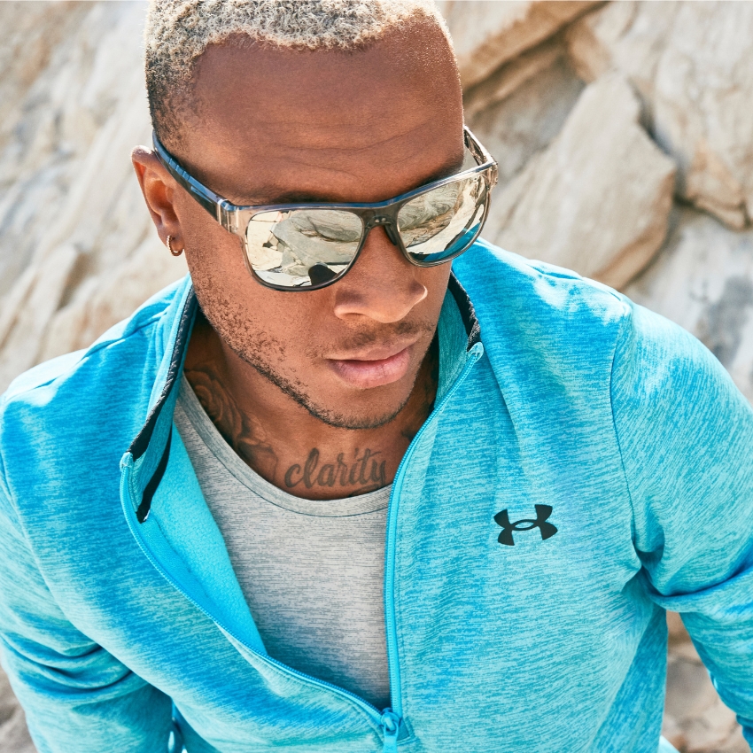 Man wearing mirrored sunglasses and a blue Under Armour zip-up jacket over a grey shirt.