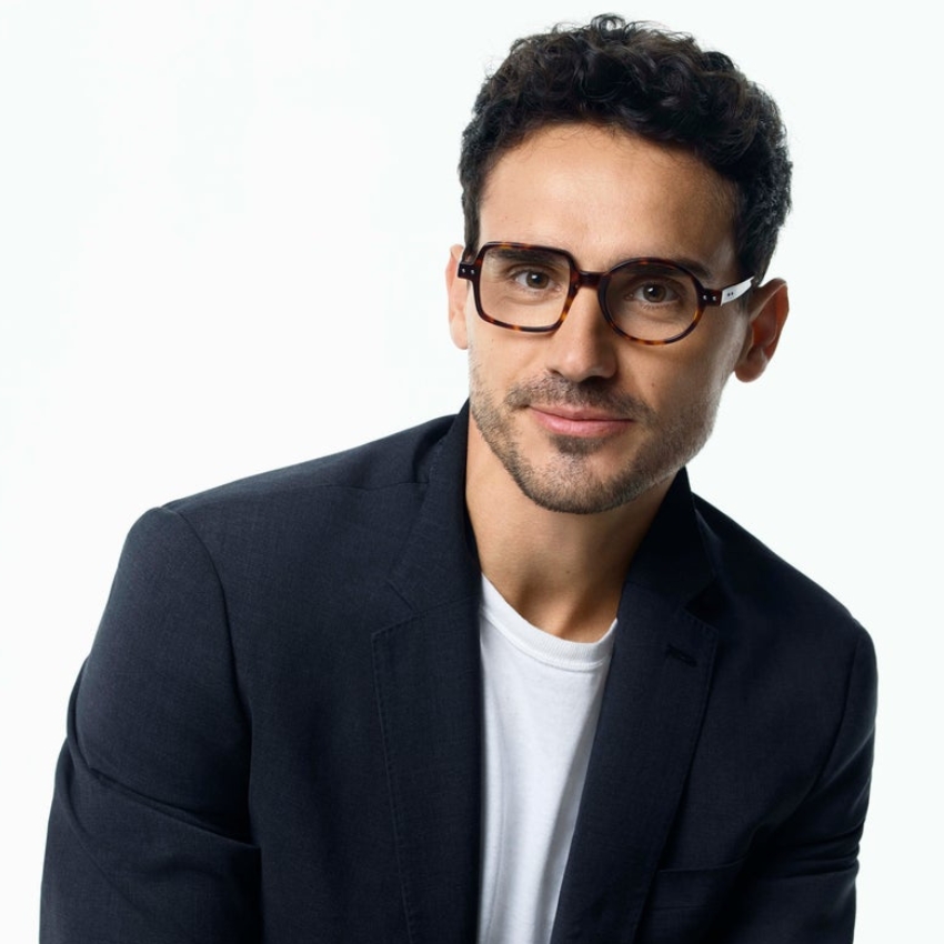 Man wearing tortoiseshell eyeglasses, a navy blazer, and a white T-shirt.