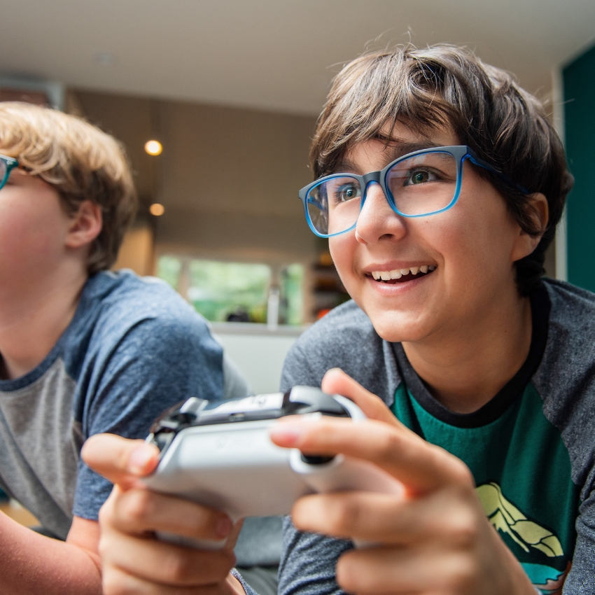 Boy wearing blue glasses playing video games with a white controller.