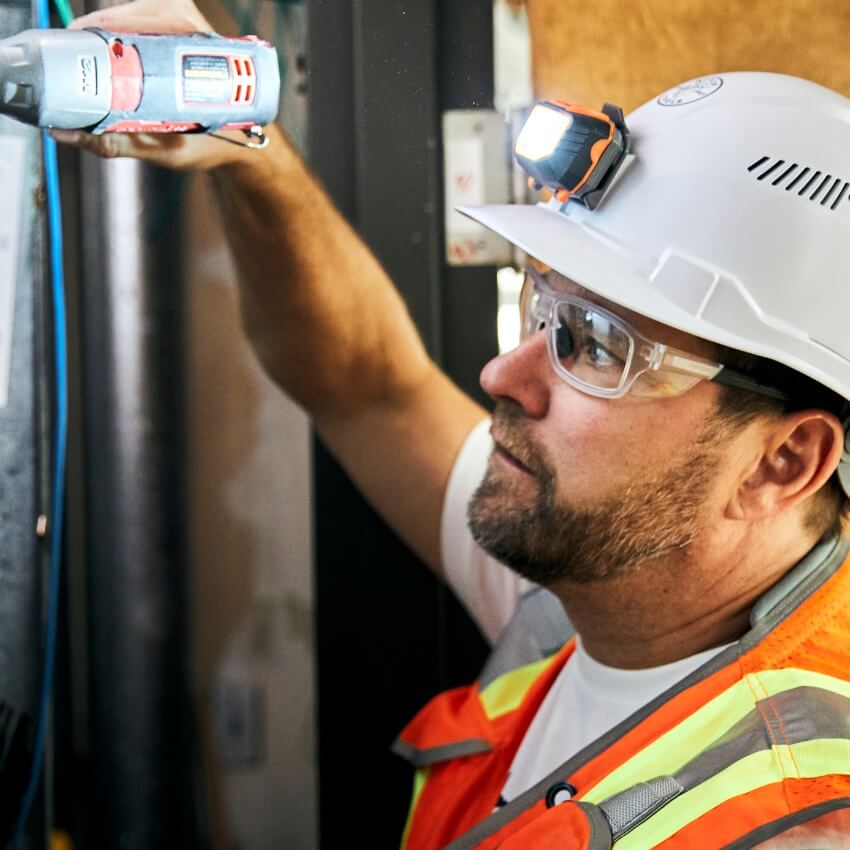 Construction worker wearing a white hard hat with LED headlamp, safety glasses, and a high-visibility vest.