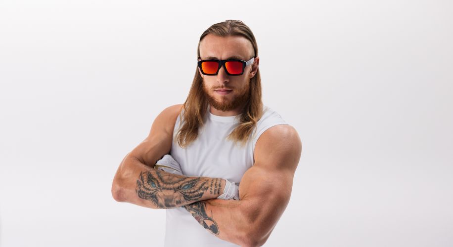 Man wearing white sleeveless shirt and mirrored red sunglasses with arms crossed.