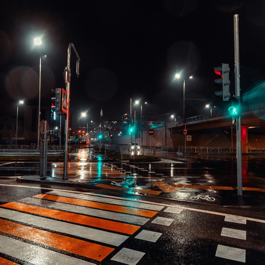 Rainy night street with illuminated crosswalk, green pedestrian signal, and wet roads reflecting streetlights.