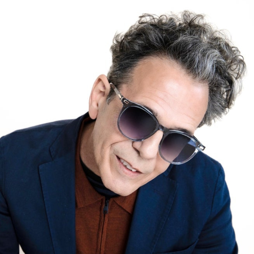 Man wearing sunglasses with gradient lenses and a dark frame. He is dressed in a navy jacket and red shirt.