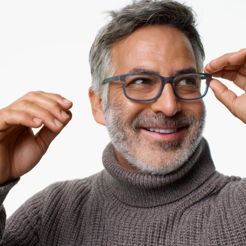 Man wearing gray rectangular eyeglasses and a gray knit turtleneck sweater, smiling and adjusting frames.