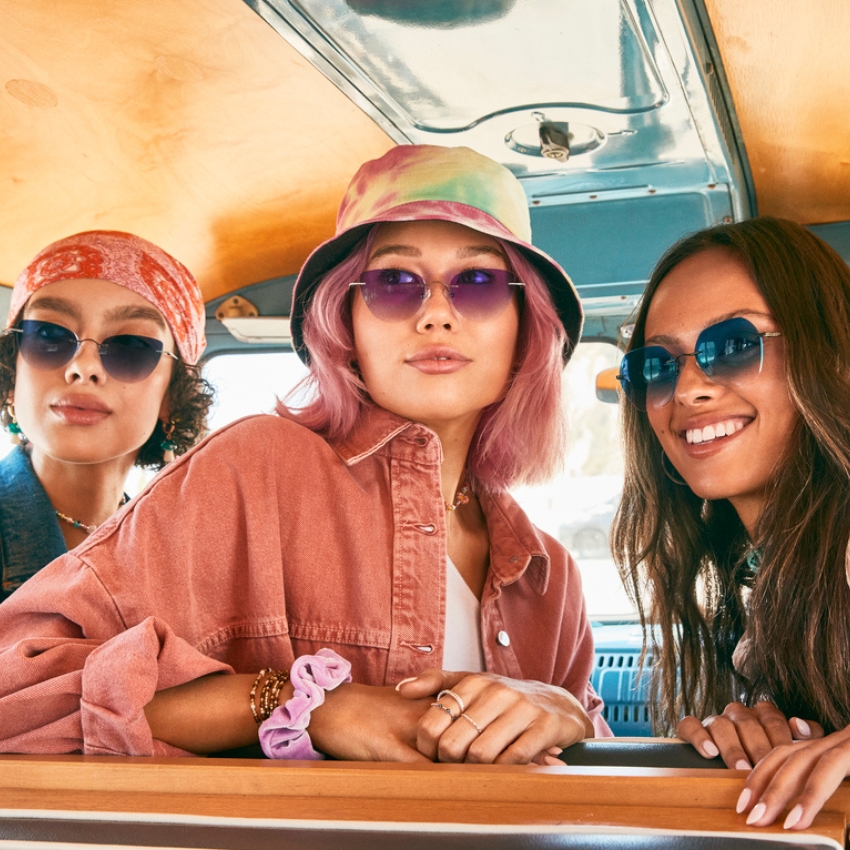 Three women wearing colorful sunglasses and stylish headwear.