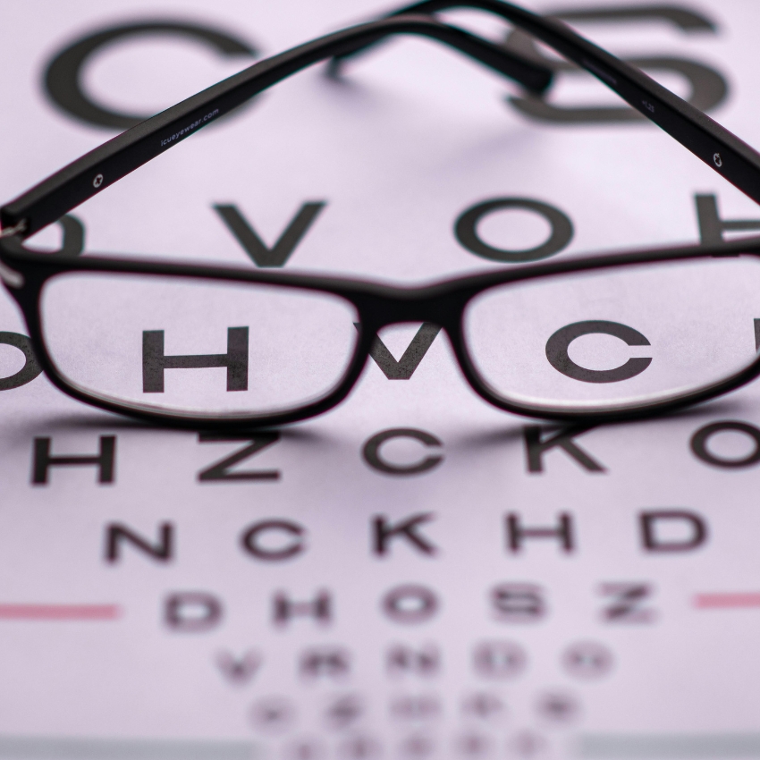 Eyeglasses resting on an eye chart, with letters "H" and "C" visible through the lenses.