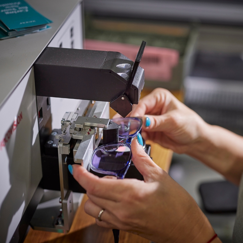 Person inspecting purple-tinted glasses using a specialized machine.