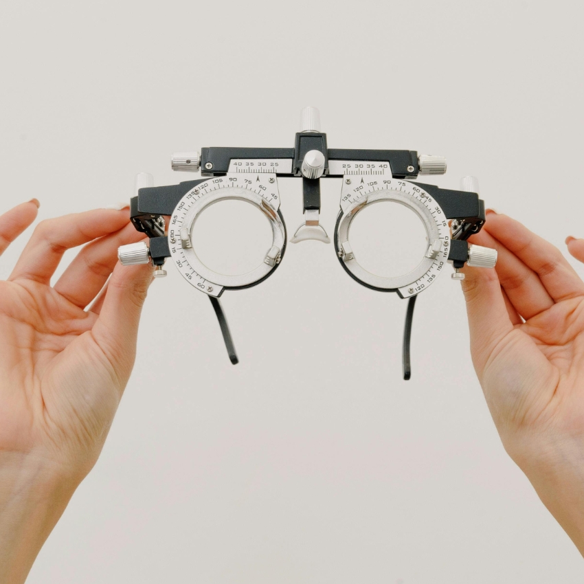 Optometry trial frame with dials and adjustments held by hands.