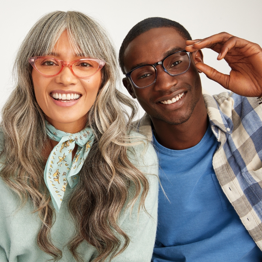 Two people smiling and wearing stylish eyeglasses; one has translucent pink frames, the other dark frames.