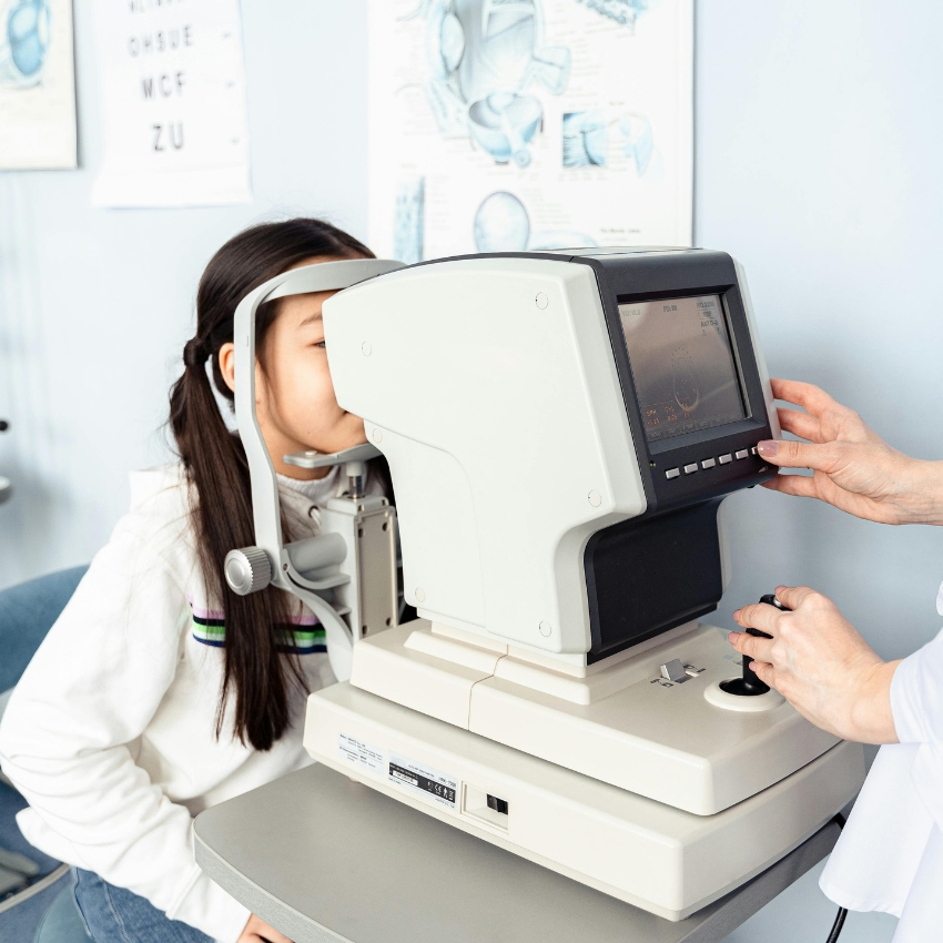 Child undergoing an eye exam using an autorefractor operated by a medical professional.